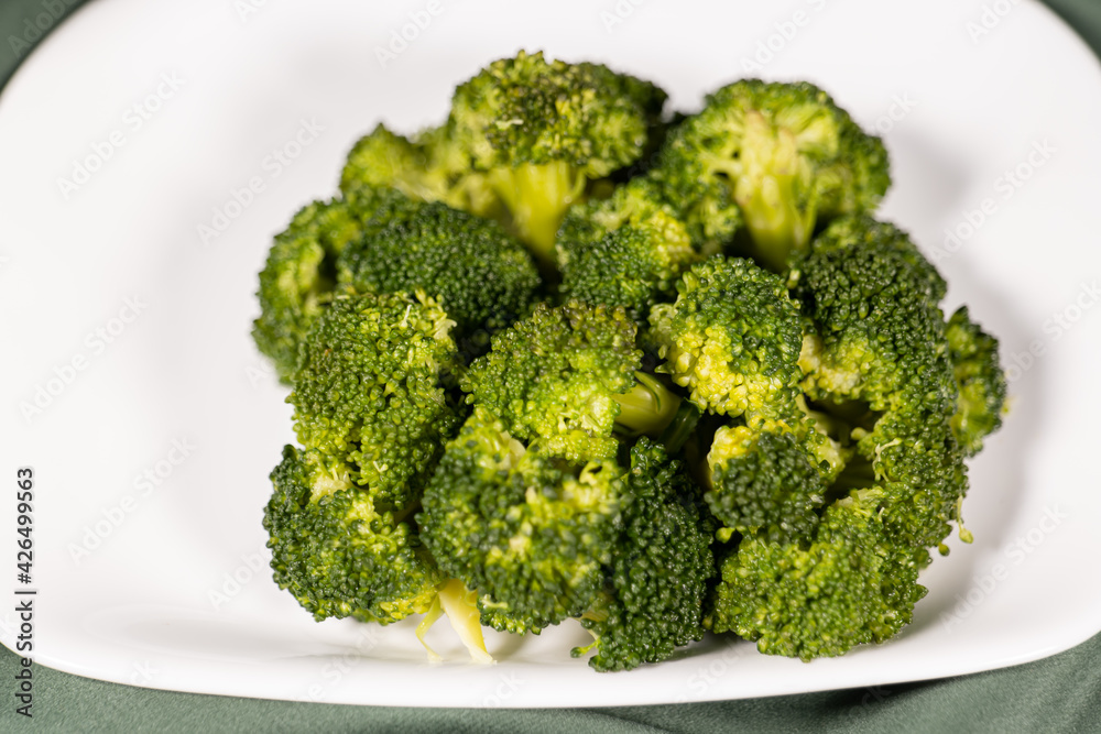 healthy food, boiled broccoli on a white plate on a dark green cloth healthy food, boiled broccoli on a white plate on a dark green cloth