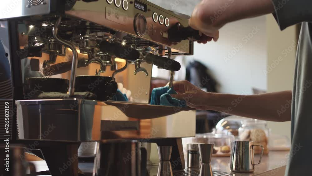 Tilt up of young male bartender wearing t-shirt and mask preparing automatic coffee machine for making next cup of fresh coffee