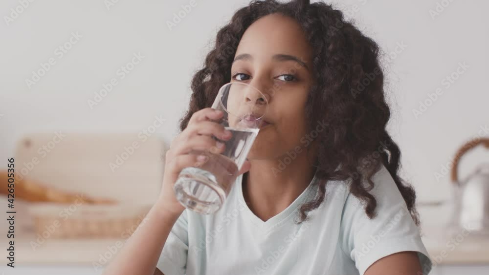 Water balance and health care. Smiling african american teen girl drinking clean water from glass and smiling to camera Water balance and health care. Smiling african american teen girl drinking clean water from glass and smiling to camera