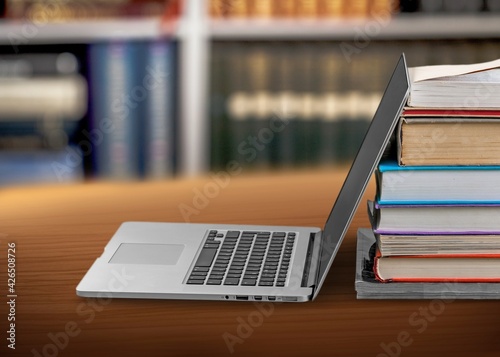 Stack of books with modern laptop on table