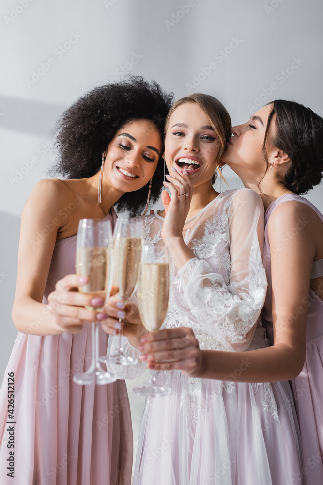 excited bride looking at camera while clinking champagne glasses with multicultural friends. excited bride looking at camera while clinking champagne glasses with multicultural friends.