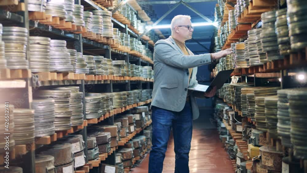 Archive specialist with a laptop is observing cases with film tape Archive specialist with a laptop is observing cases with film tape