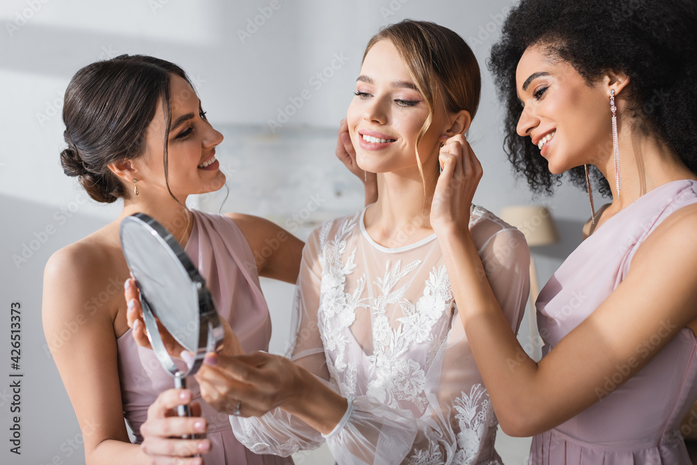 young bride looking in mirror near interracial friends preparing her for wedding. young bride looking in mirror near interracial friends preparing her for wedding.