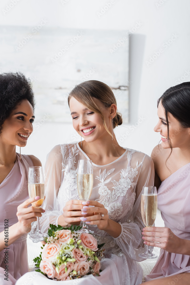 multicultural bridesmaids looking at happy bride while holding champagne glasses. multicultural bridesmaids looking at happy bride while holding champagne glasses.