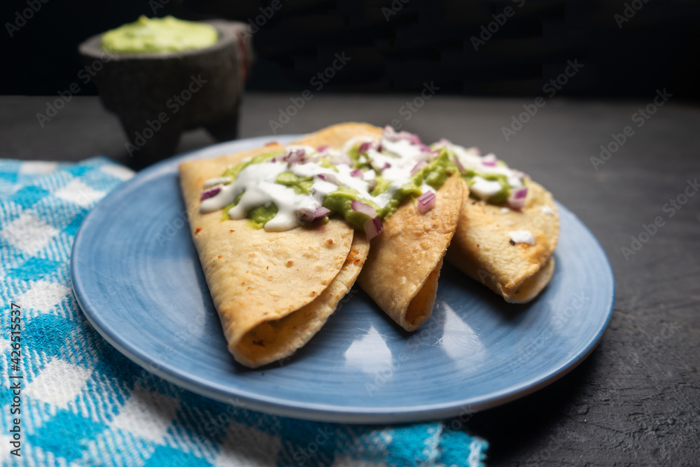 Fried tacos with guacamole and sour cream on dark background. Mexican food