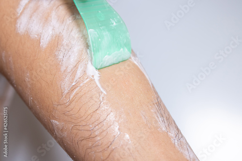 Woman epilating leg with depilation cream and spatula.