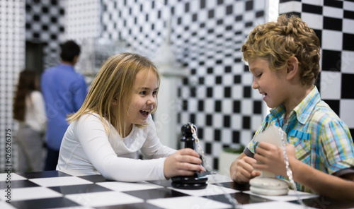 Cheerful interested tweens trying to get out of escape room stylized under chessboard