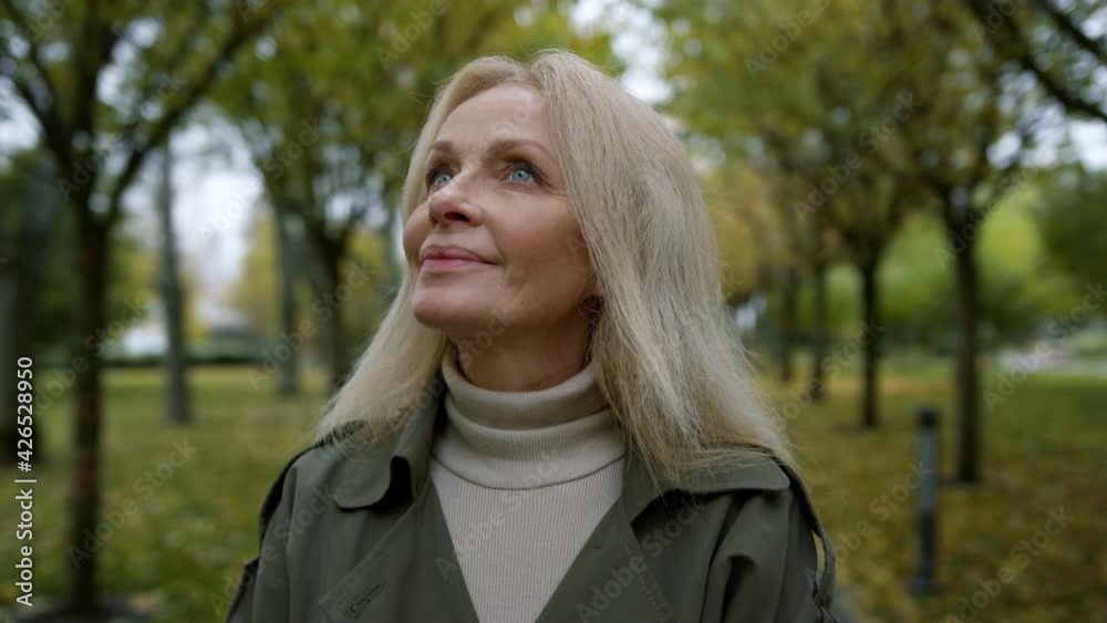 Portrait of romantic woman looking into sky through trees branches in park .