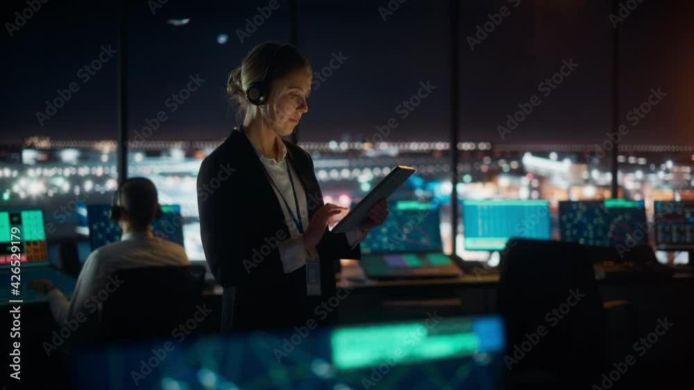 Caucasian Female Air Traffic Controller Working on Tablet in Airport Tower. Office Room is Full of Desktop Computer Displays with Navigation Screens, Airplane Flight Radar Data for the Team.