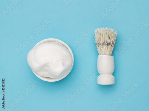 Fotografi Shaving foam in a white bowl and a white shaving brush on a blue background