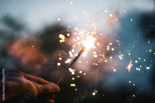 Bright sparkler in a male hand in the blurred background