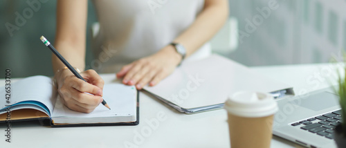 Close up view of young female hand with pencil writing on notebook while doing homework