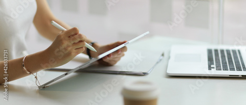 Side view of female hand working with digital tablet on workspace