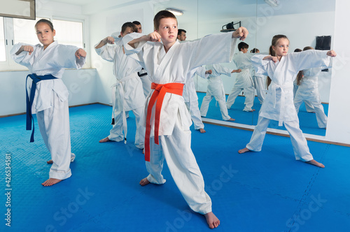 Young children training karate kicks with male coach during karate class.