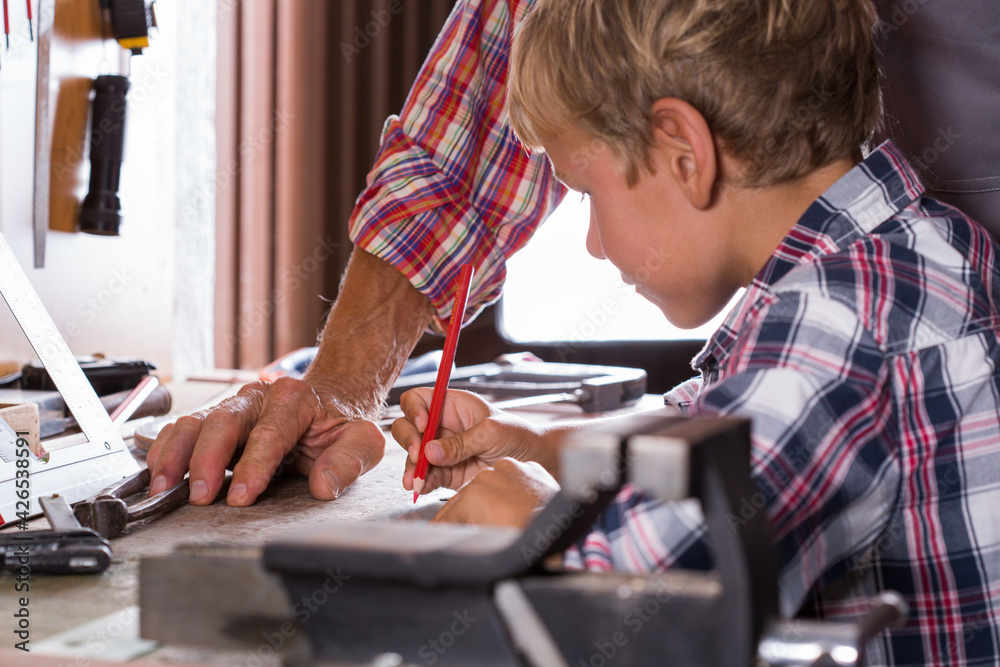 Grandfather teaches boy to work on bench with joinery tools