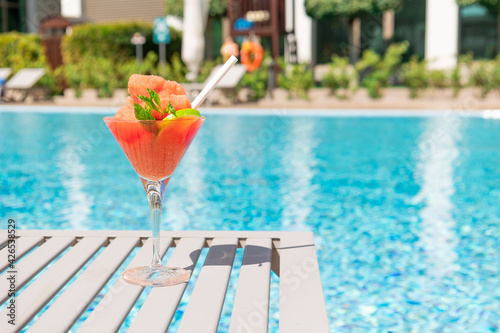 Fresh red cocktail with ice in glass on swimming pool. Tropical juice on luxury vacations. Concept summer holiday and travel