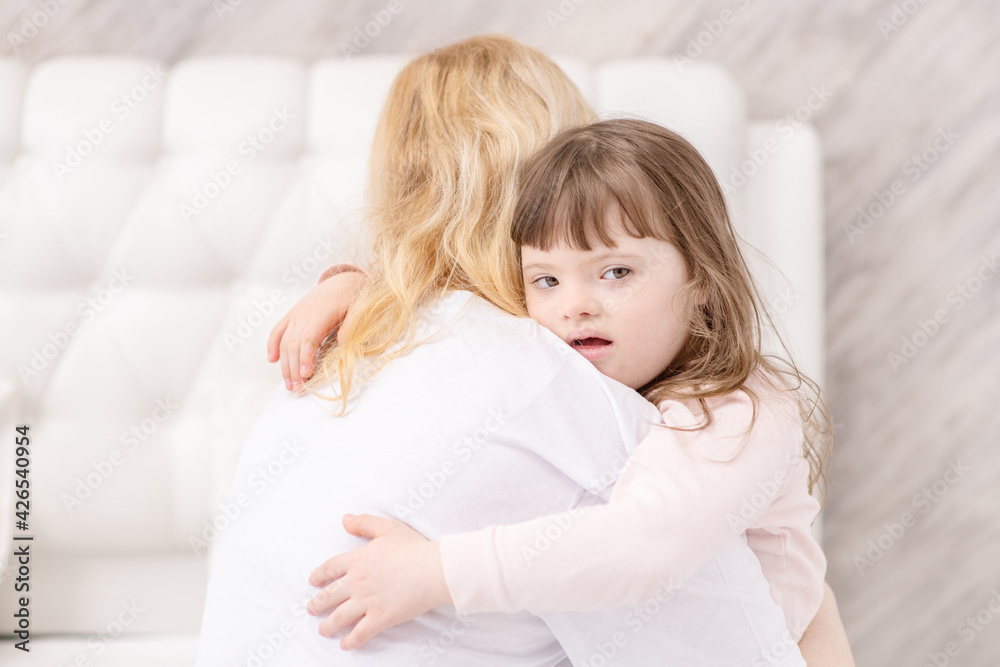 Mom hugging a girl with down syndrome at home in the bedroom on the bed. Ordinary childcare in a family for children with disabilities Mom hugging a girl with down syndrome at home in the bedroom on the bed. Ordinary childcare in a family for children with disabilities