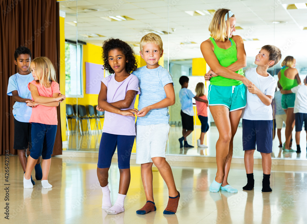 Group of preteen children training movements of slow foxtrot in dance studio with female tutor