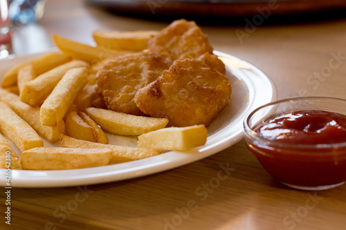 Chicken nuggets with French fries and tomato sauce. Fried chicken nuggets with potatoes and ketchup close-up. Artistically blurry. Wrong tasty food