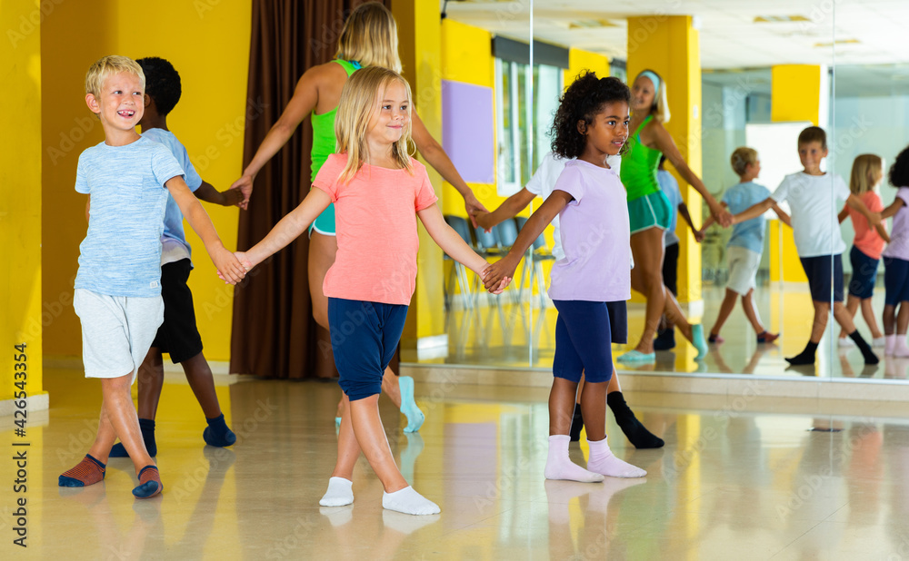 Happy kids and female teacher dancing together in studio at elementary school. High quality photo