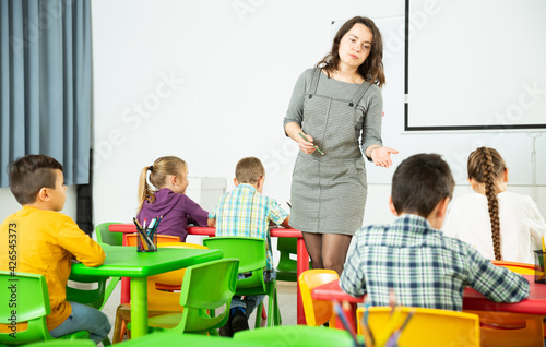 Friendly smiling teacher explaining studying material to children during lesson at elementary school