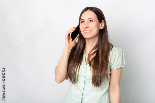 Photo of young charming woman smiling and talking on phone near white background