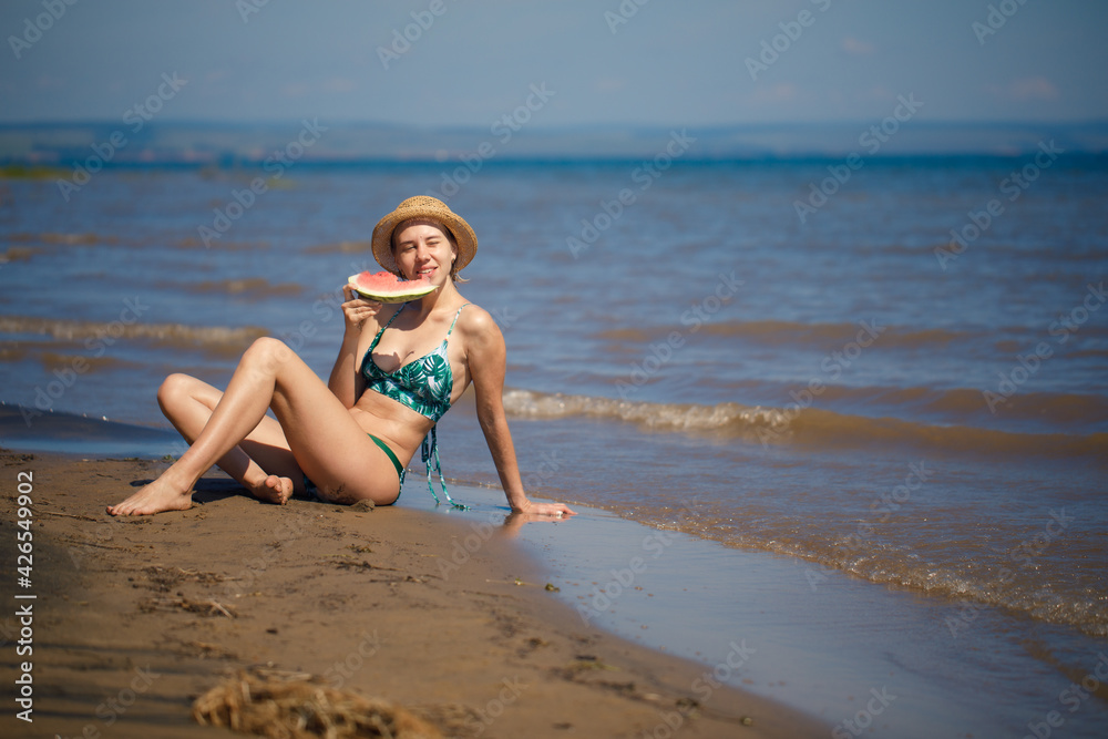 Portrait of smiling woman relaxing holding and eating a slice of watermelon on the tropical beach Portrait of smiling woman relaxing holding and eating a slice of watermelon on the tropical beach