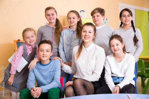 Portrait of friendly smiling group of pupils with female teacher sitting in schoolroom