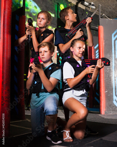 Group portrait of happy teenagers with laser guns having fun on dark lasertag arena..