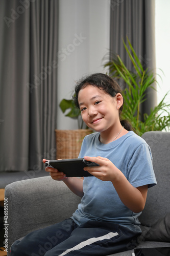 Portrait of happy little girl playing video game while sitting on couch at home.