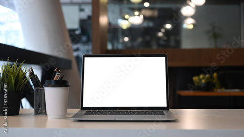 Mock up laptop computer with blank screen, coffee cup, pencil holder and plant on white table in office. © Prathankarnpap