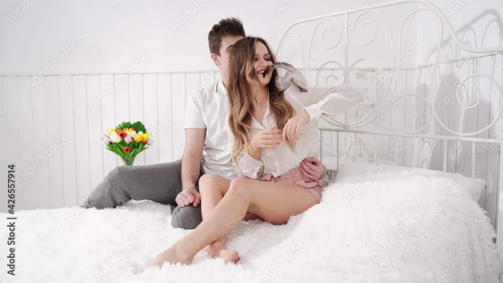A beautiful couple of young lovers holding a small white kitten sitting in bed 