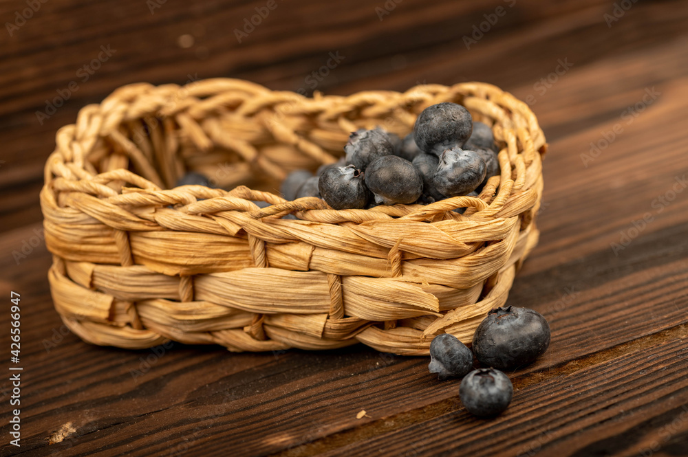 Obraz premium Fresh blueberries in a wicker basket on a wooden table. Harvest, village breakfast.