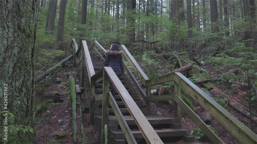 Girl Walking on a Beautiful Path in the Rainforest during a wet and rainy day. Lynn Canyon Park, North Vancouver, British Columbia, Canada. Girl Walking on a Beautiful Path in the Rainforest during a wet and rainy day. Lynn Canyon Park, North Vancouver, British Columbia, Canada.