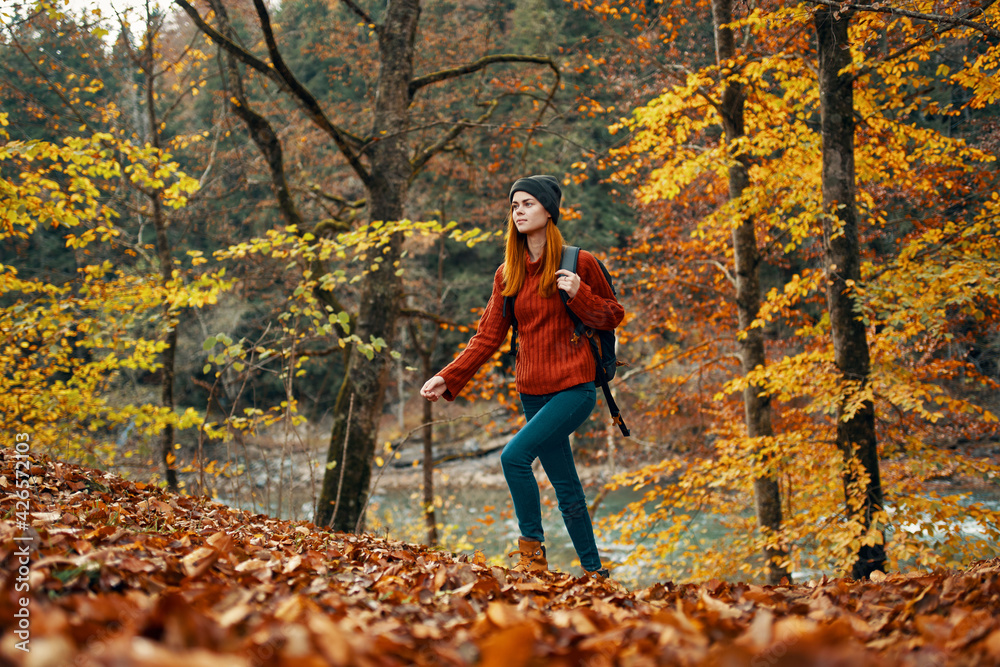 woman tourist walks through the park in autumn with a backpack on her back and tall trees landscape river lake woman tourist walks through the park in autumn with a backpack on her back and tall trees landscape river lake