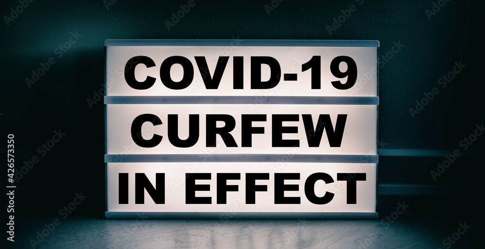Fototapeta premium Curfew in effect text message on lit lightbox for covid coronavirus pandemic. Warning at night.