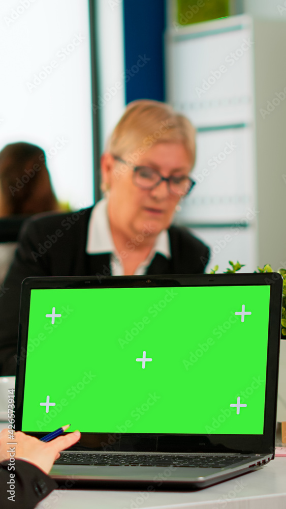 Over the sholder of manager sitting at meeting desk looking at laptop with green screen mockup while diverse team working on background. Multiethnic people planning project on chroma key display Over the sholder of manager sitting at meeting desk looking at laptop with green screen mockup while diverse team working on background. Multiethnic people planning project on chroma key display