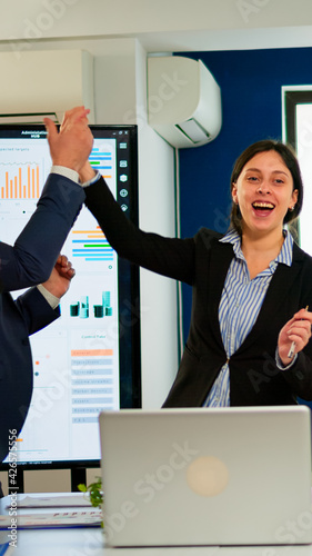 Happy diverse businesspeople designers giving high five during team corporate brainstorm receving good news. Multiethnical partners coworkers celebrate successful teamwork result at company briefing photo