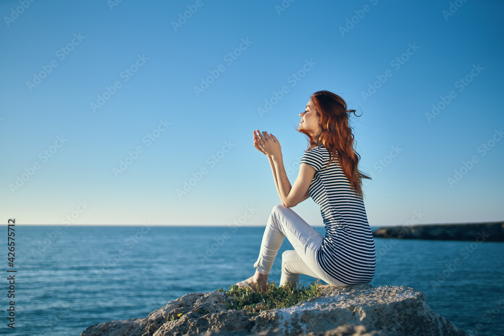 happy woman in t-shirt trousers sits on a large stone near the sea in summer happy woman in t-shirt trousers sits on a large stone near the sea in summer