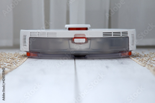 White robot vacuum cleaner effectively removes grain from the laminate leaving a clean path behind