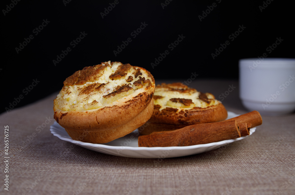 Two muffins with cottage cheese and cinnamon on a white plate. close-up. Two cinnamon sticks.