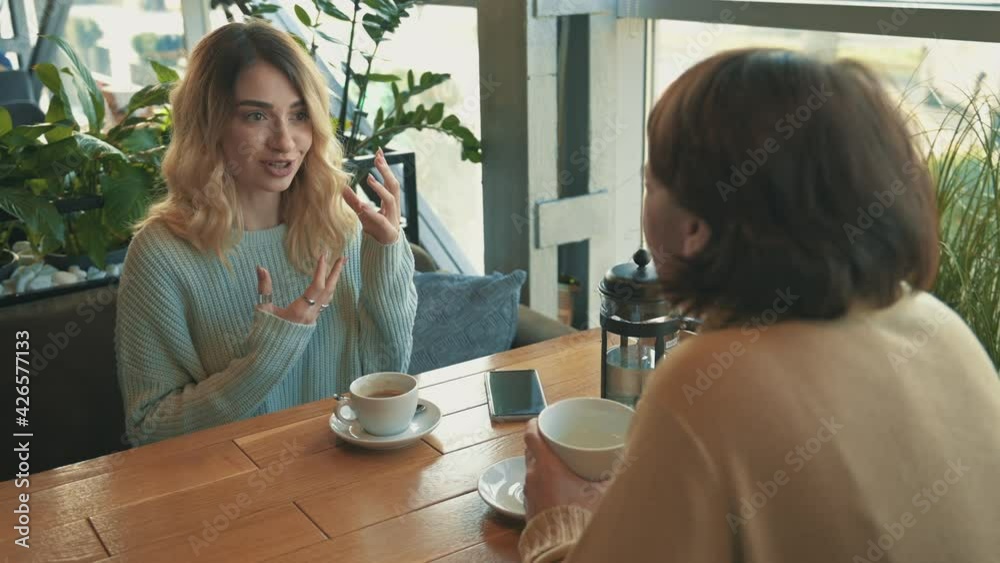 Young female friends talking and having a cup of tea and a coffee Young female friends talking and having a cup of tea and a coffee