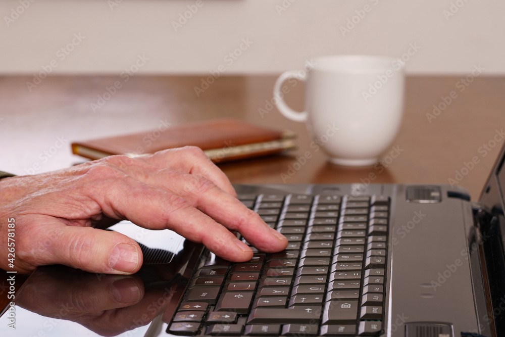Close-up hand on laptop keyboard. Blurred white cup on a background. Close-up hand on laptop keyboard. Blurred white cup on a background.