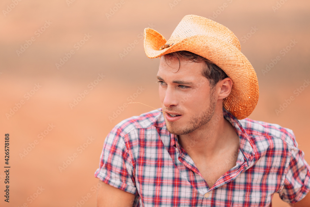 Cowboy man wearing western hat with straw in mouth in country farm background. Happy American Male model in american countryside landscape nature on ranch or farm, Utah, USA.