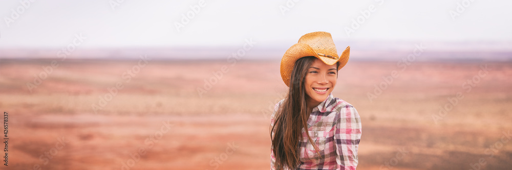 Cowgirl woman smiling happy on country farm landscape wearing cowboy hat. Banner of young multiracial Asian American girl in panoramic countryside.