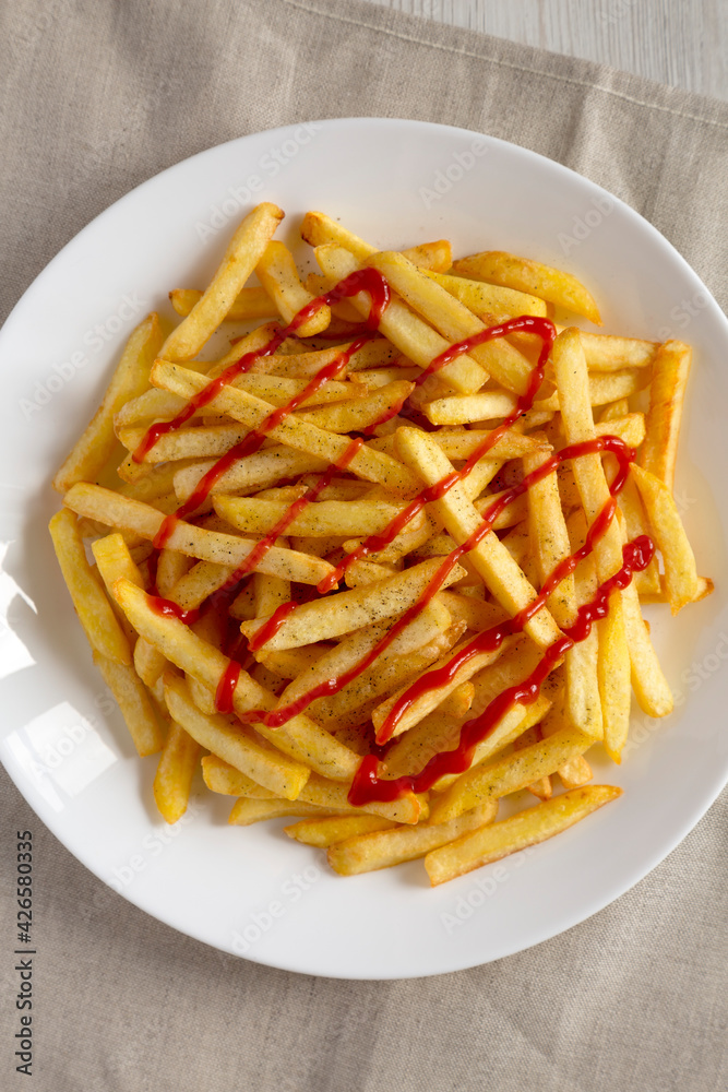 Homemade French Fries with Ketchup, Salt and Pepper on a white plate on a white wooden background, top view. Flat lay, overhead, from above. Close-up. Homemade French Fries with Ketchup, Salt and Pepper on a white plate on a white wooden background, top view. Flat lay, overhead, from above. Close-up.
