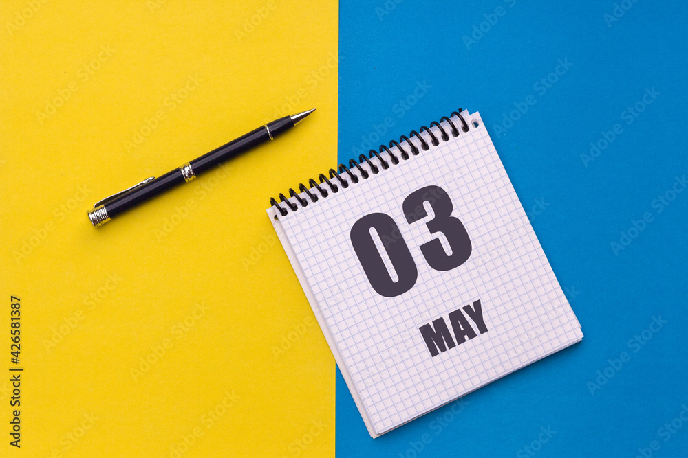 May 3rd. Day 3 of month. calendar date. Notebook with a spiral and pen lies on a yellow-blue background May 3rd. Day 3 of month. calendar date. Notebook with a spiral and pen lies on a yellow-blue background
