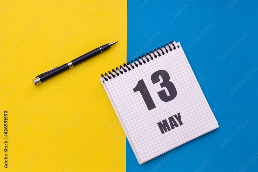 May 13th. Day 13 of month, calendar date. Notebook with a spiral and pen lies on a yellow-blue background May 13th. Day 13 of month, calendar date. Notebook with a spiral and pen lies on a yellow-blue background