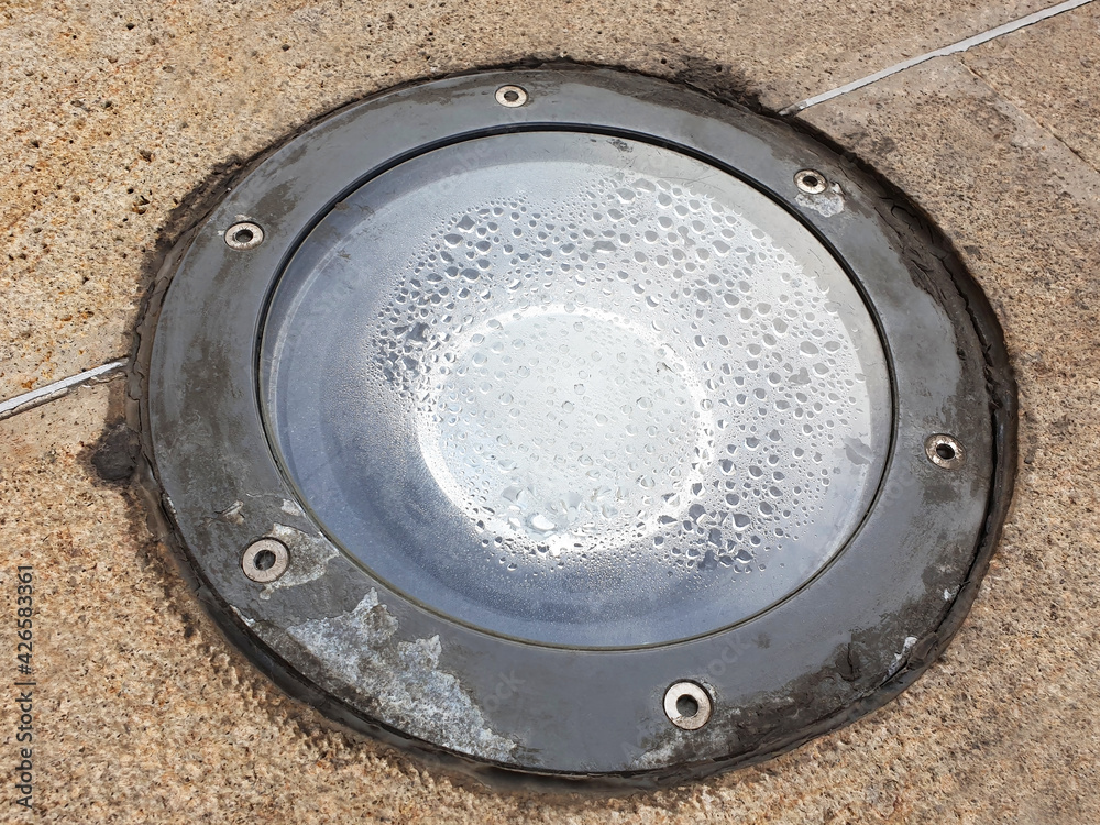 Round old lighting in the sidewalk with condensation after the rain.