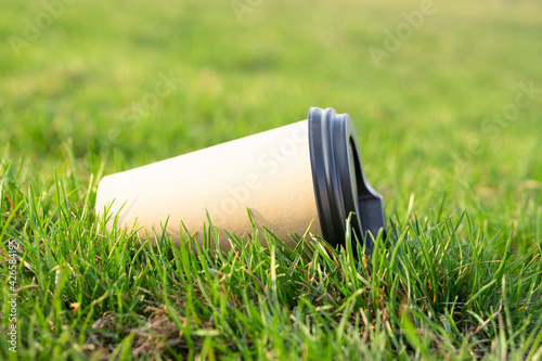 A paper coffee cup is thrown into the green grass. Environmental pollution with household waste.